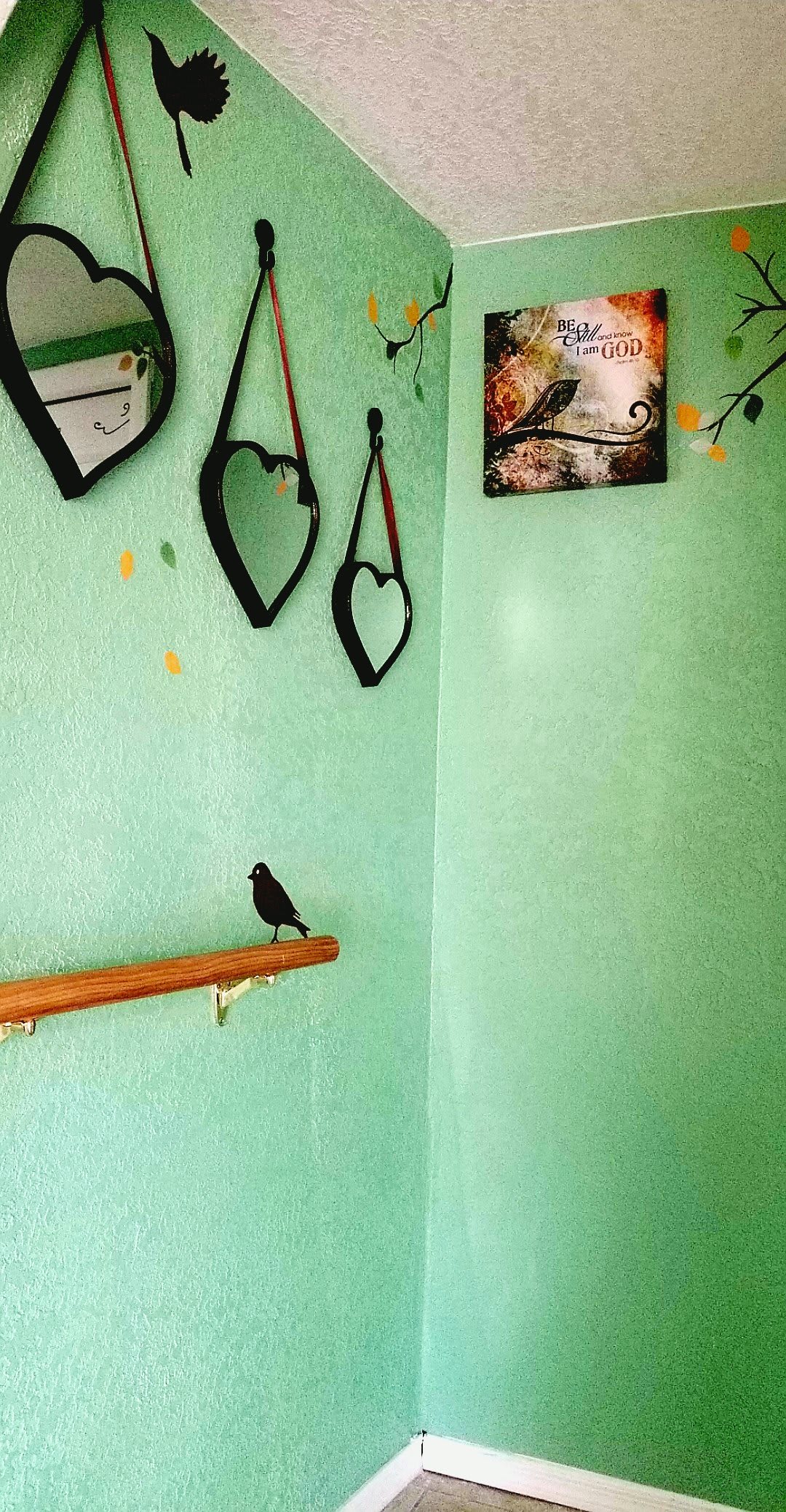 A cozy room corner with heart-shaped mirrors, a bird figurine on a wooden ledge, and a serene artwork against green walls.