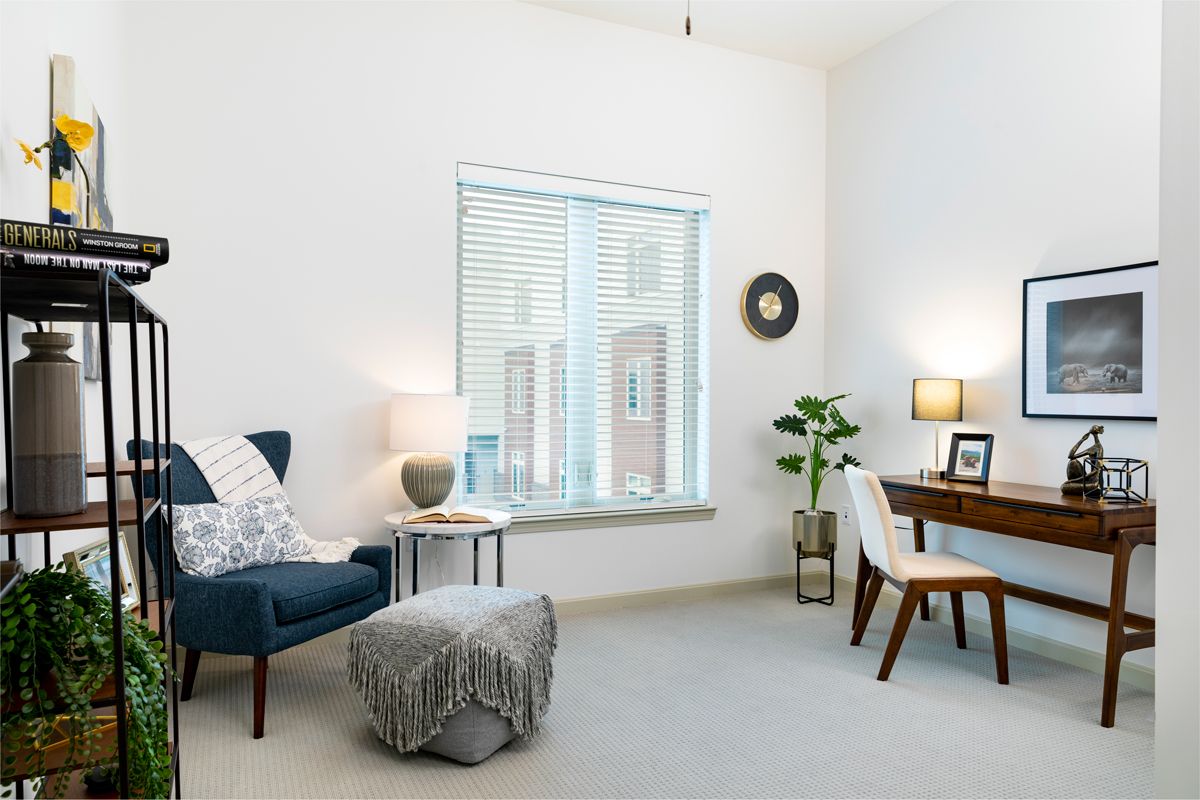 A minimalist living room with a cozy reading chair, desk area, and abundant natural light from the window.