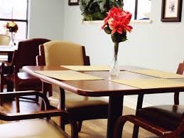 A dining table with a vase of red flowers.