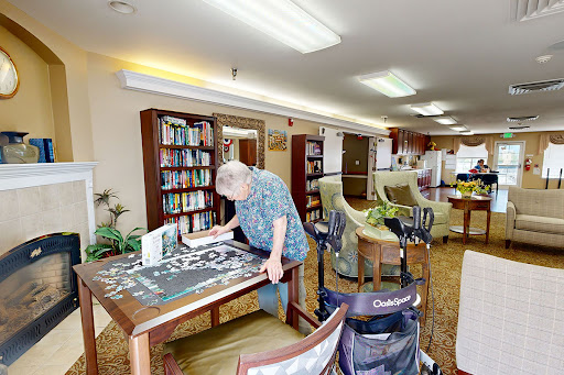 A senior individual engaged in a puzzle activity in a cozy, well-lit community space with bookshelves and comfortable seating.