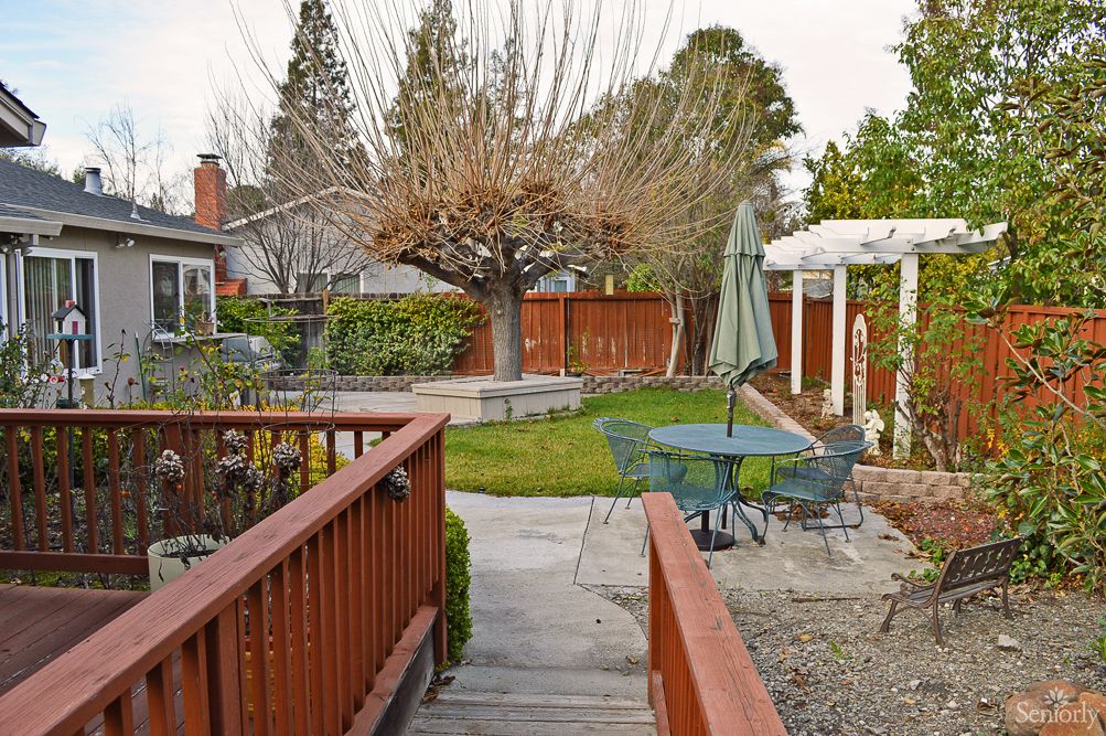A cozy backyard with a patio, garden furniture, and a grassy area surrounded by trees.