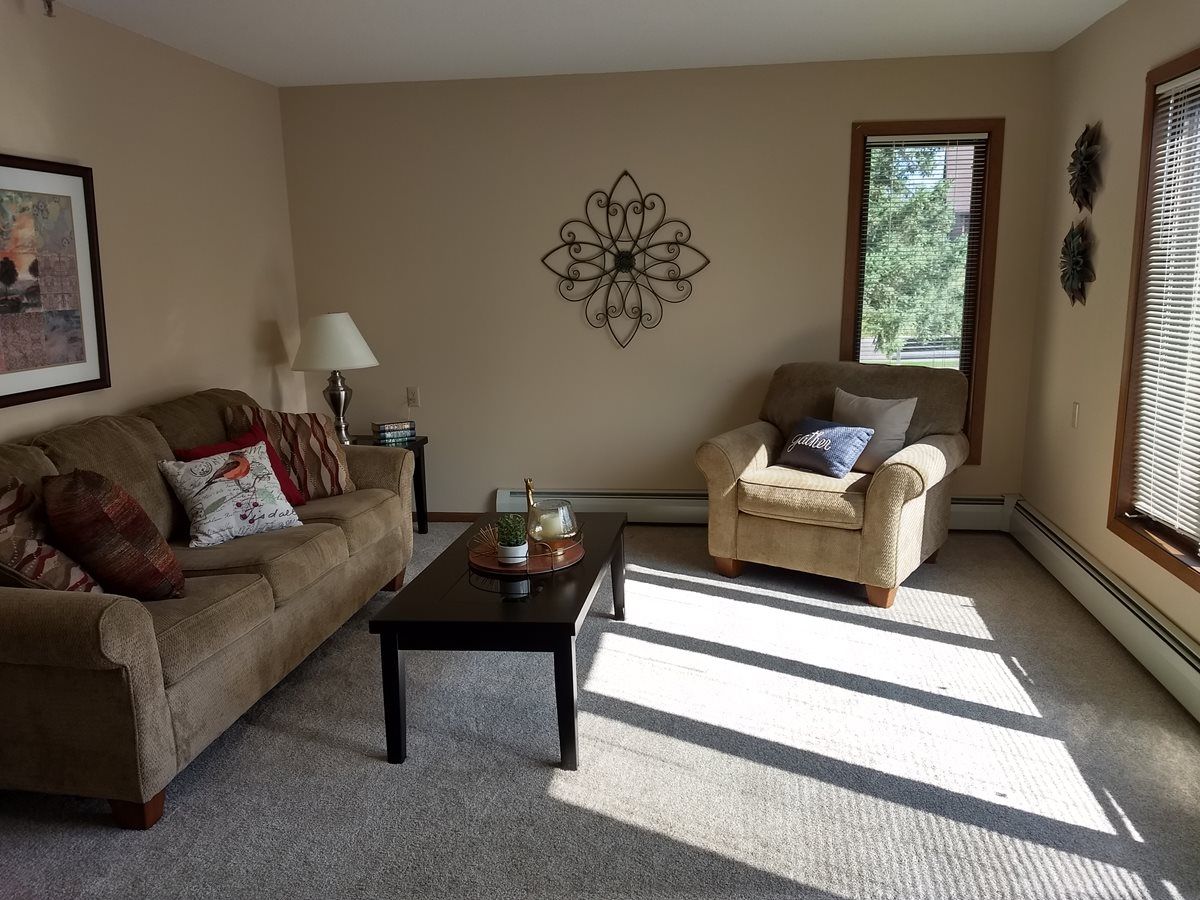 A cozy living room with a sofa, armchair, and coffee table, bathed in natural light from a window.