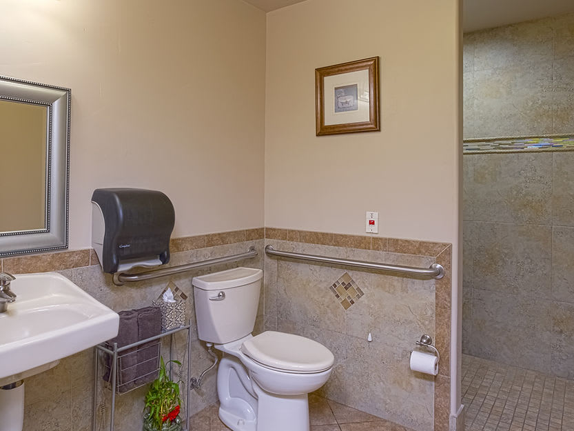 A clean, well-lit bathroom with a toilet, sink, and paper towel dispenser.