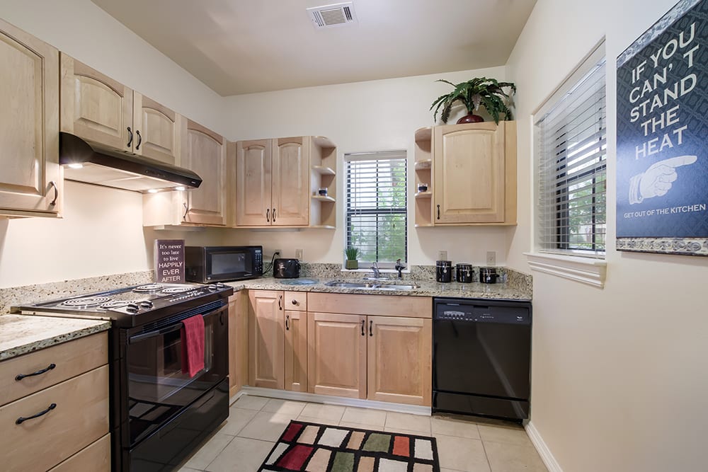 A modern, compact kitchen with light wood cabinets and black appliances.