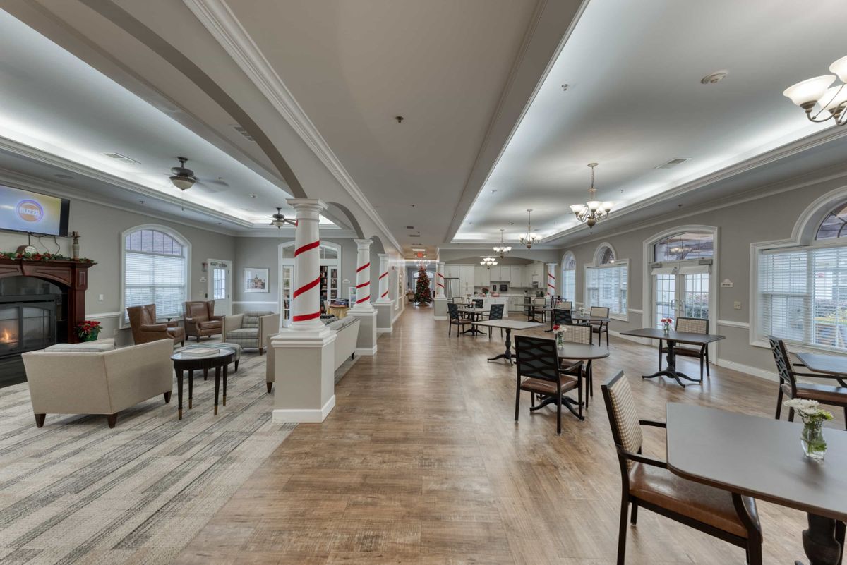 A spacious and well-lit dining area with wooden floors, arranged chairs and tables, and ceiling lights.