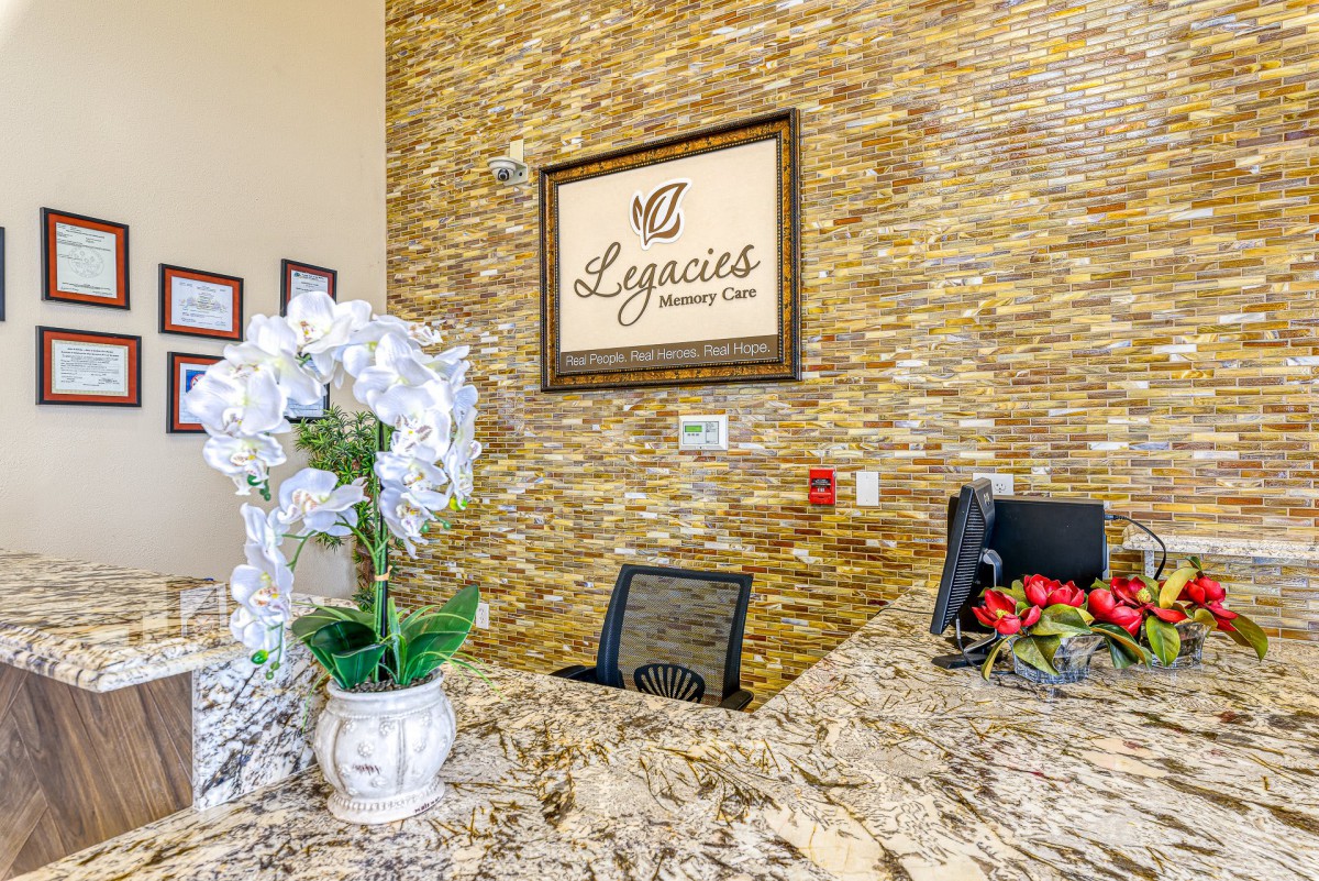 A well-decorated reception area featuring a marble desk, floral arrangement, and a prominent sign on a textured wall.