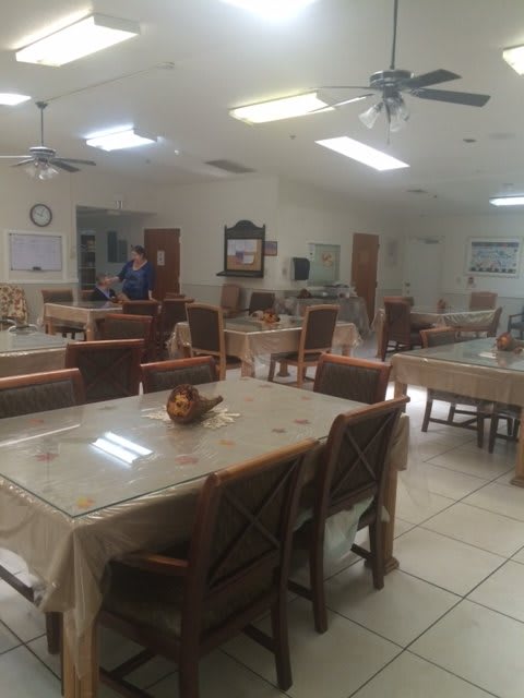 A spacious dining area with multiple tables and chairs, illuminated by fluorescent lights.