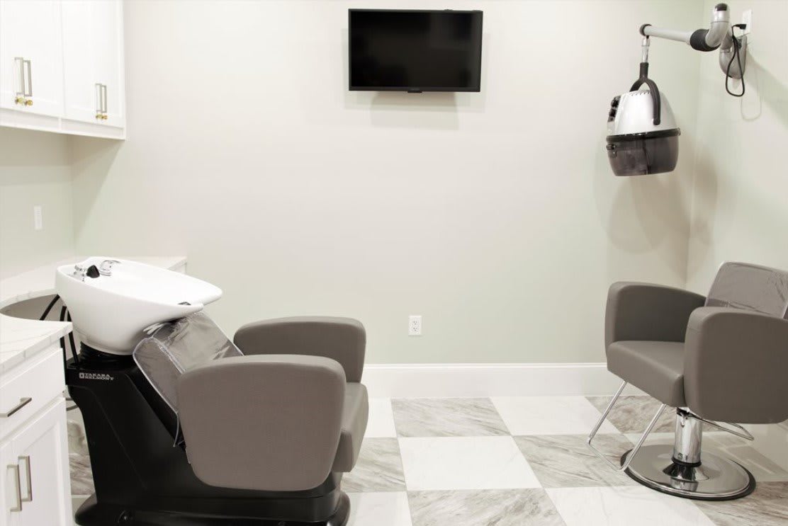 A modern hair salon interior with chairs and a television on the wall.