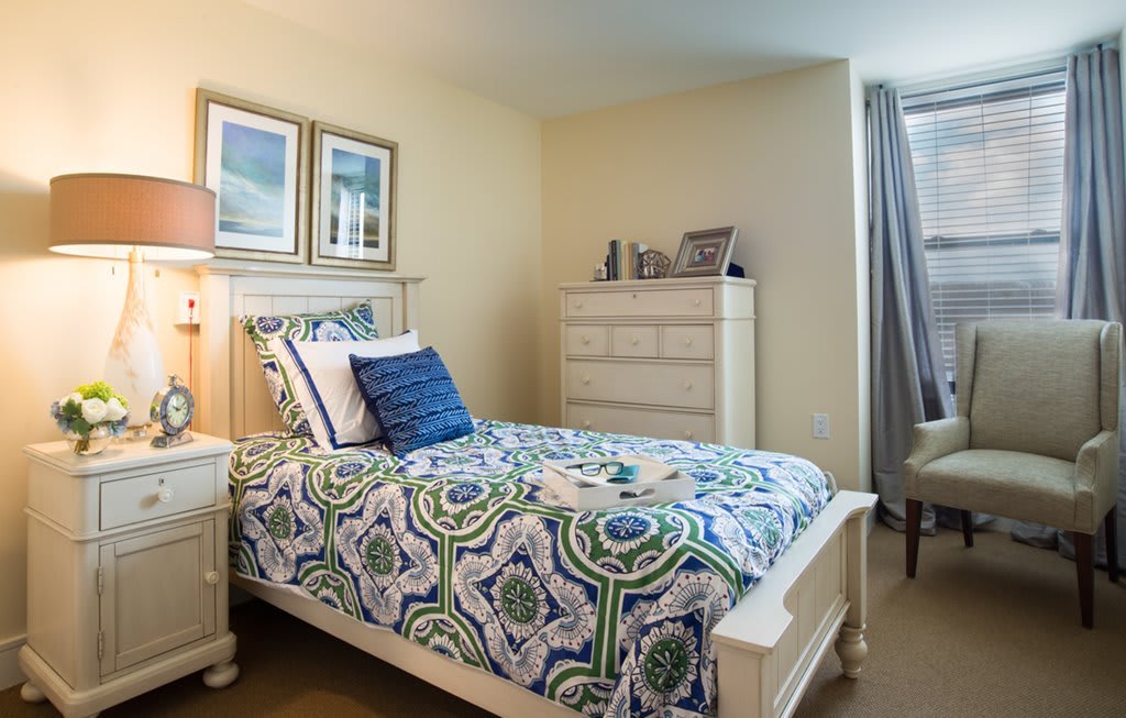 A cozy bedroom with a patterned bedspread, white furniture, and framed wall art.