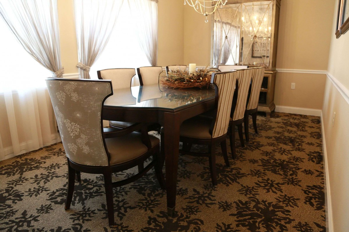 An elegantly decorated dining room featuring a large table with cushioned chairs, a chandelier, and patterned carpet.