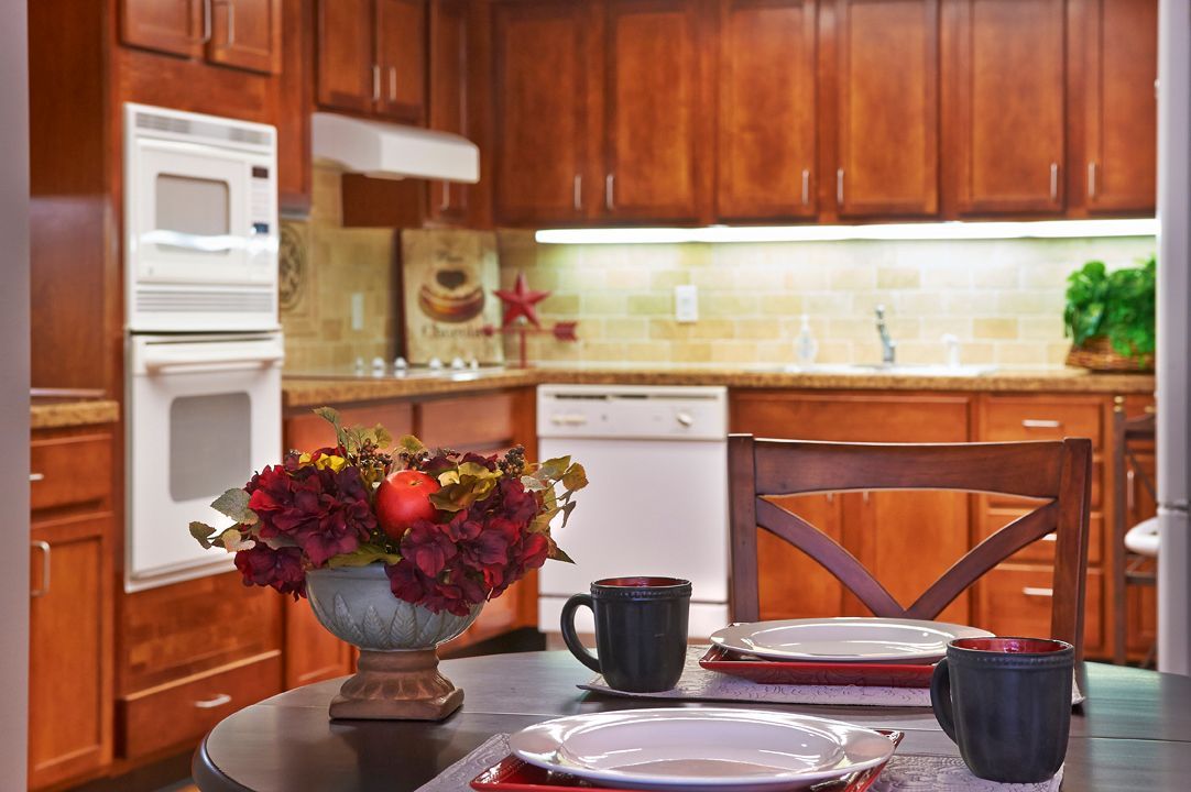 A cozy kitchen with wooden cabinets, a dining table set with plates and mugs, and a flower arrangement centerpiece.