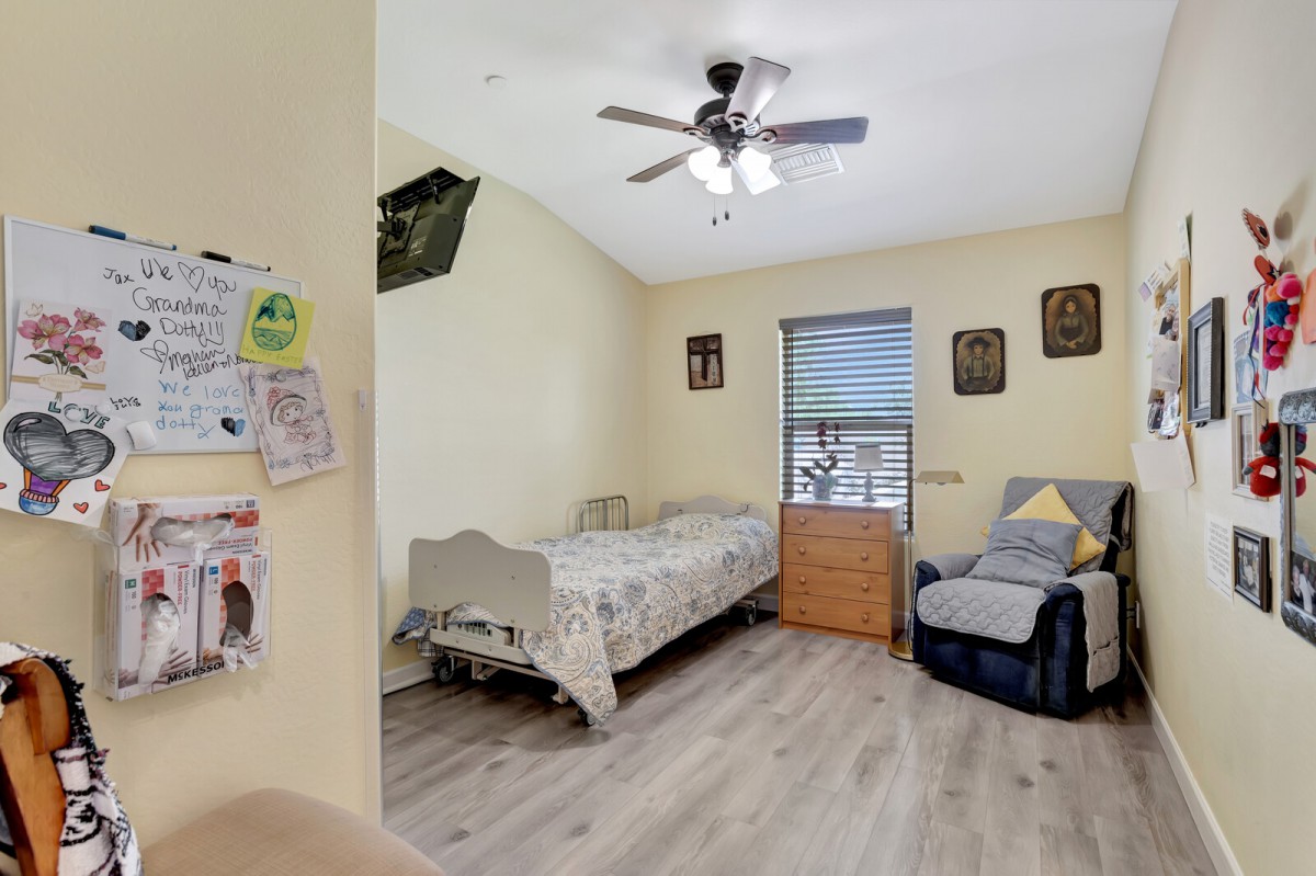 A cozy bedroom with a single bed, armchair, and ceiling fan.