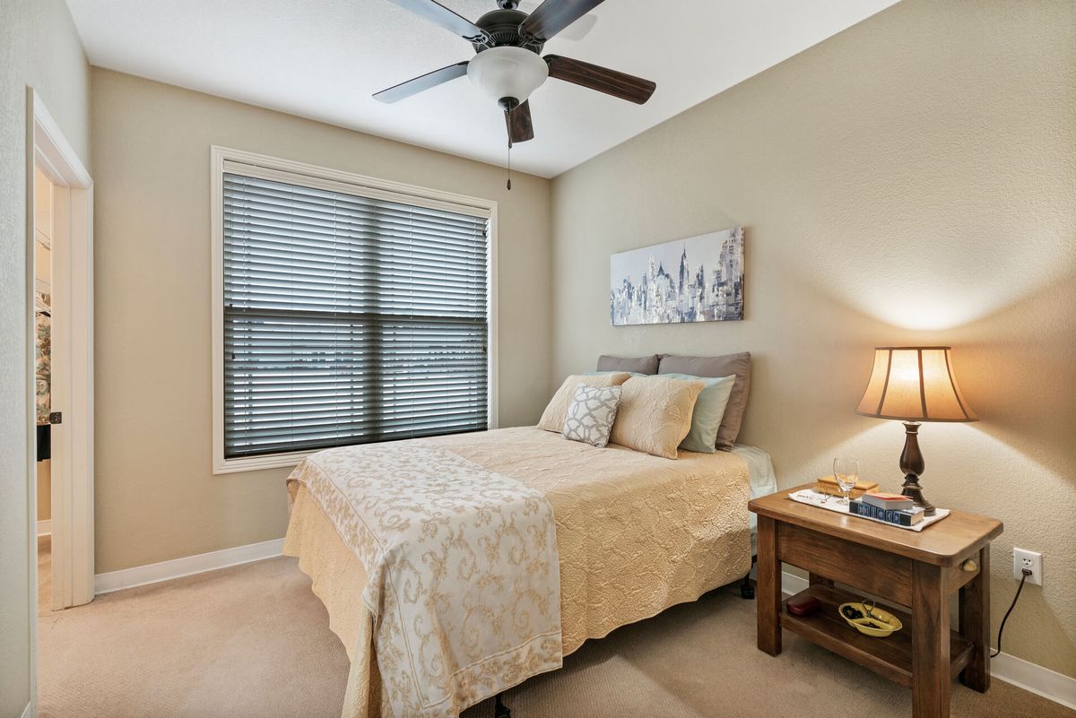 A cozy bedroom with a neatly made bed, ceiling fan, and a window with blinds.