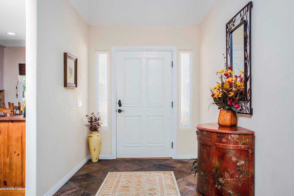 A well-decorated entryway with a white front door, vase of flowers, and ornate mirror.
