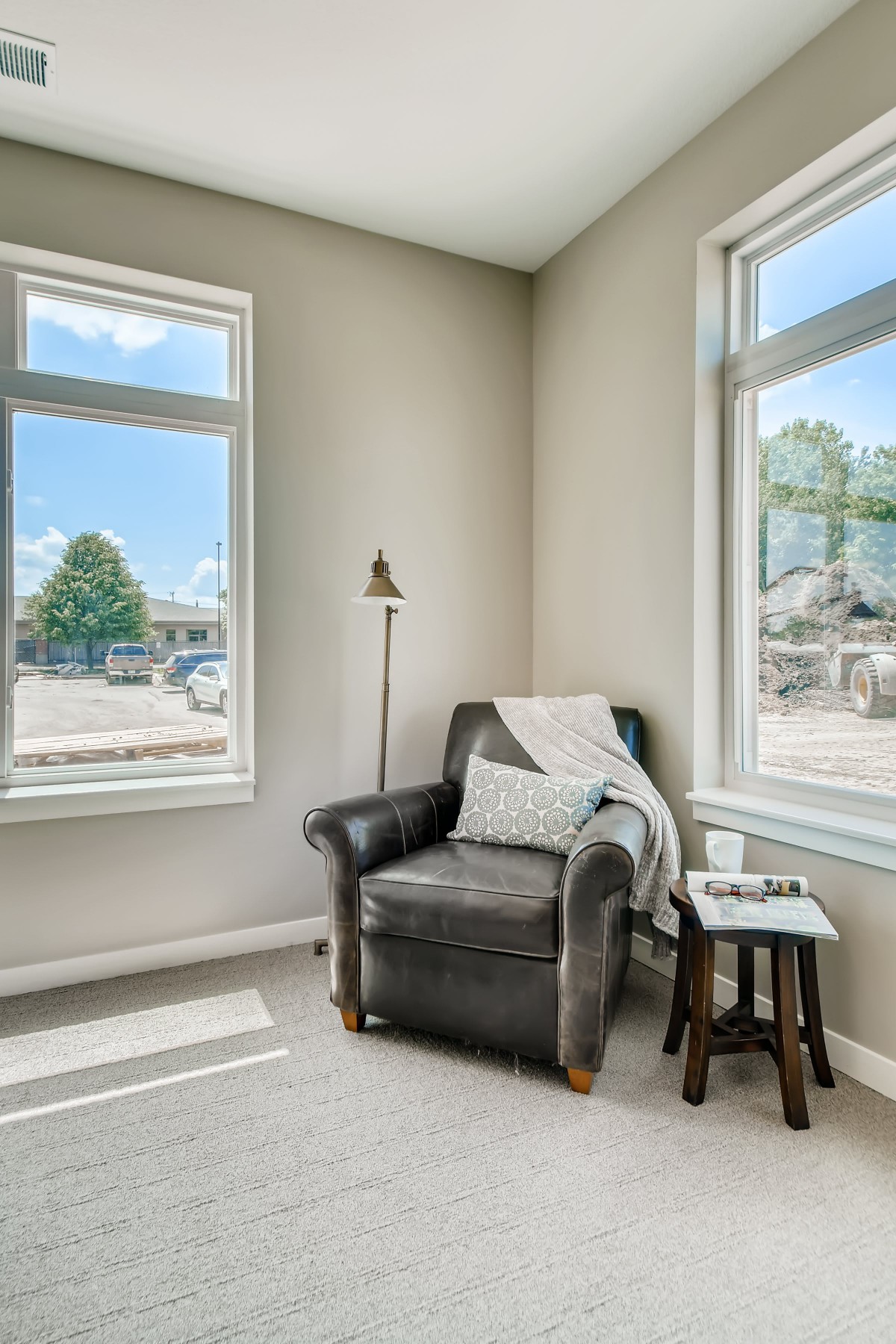 A cozy living room corner featuring a black leather armchair and a side table, bathed in natural light from large windows.