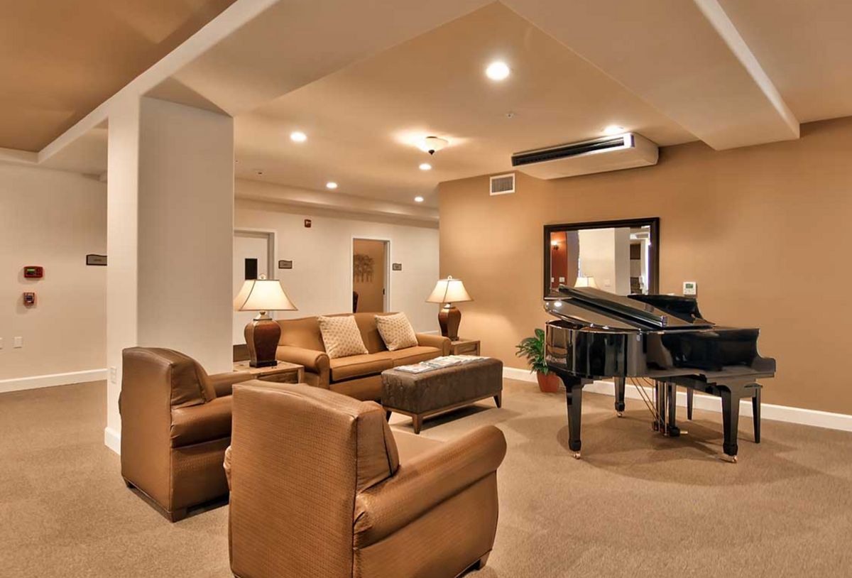 A modern living room featuring a grand piano, leather seating, and warm lighting.