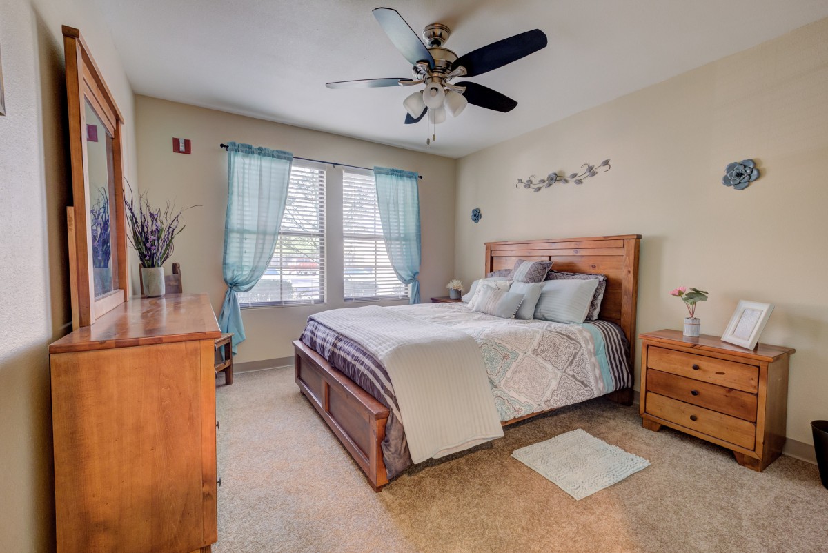 A cozy bedroom with a wooden bed frame, blue curtains, and a ceiling fan.