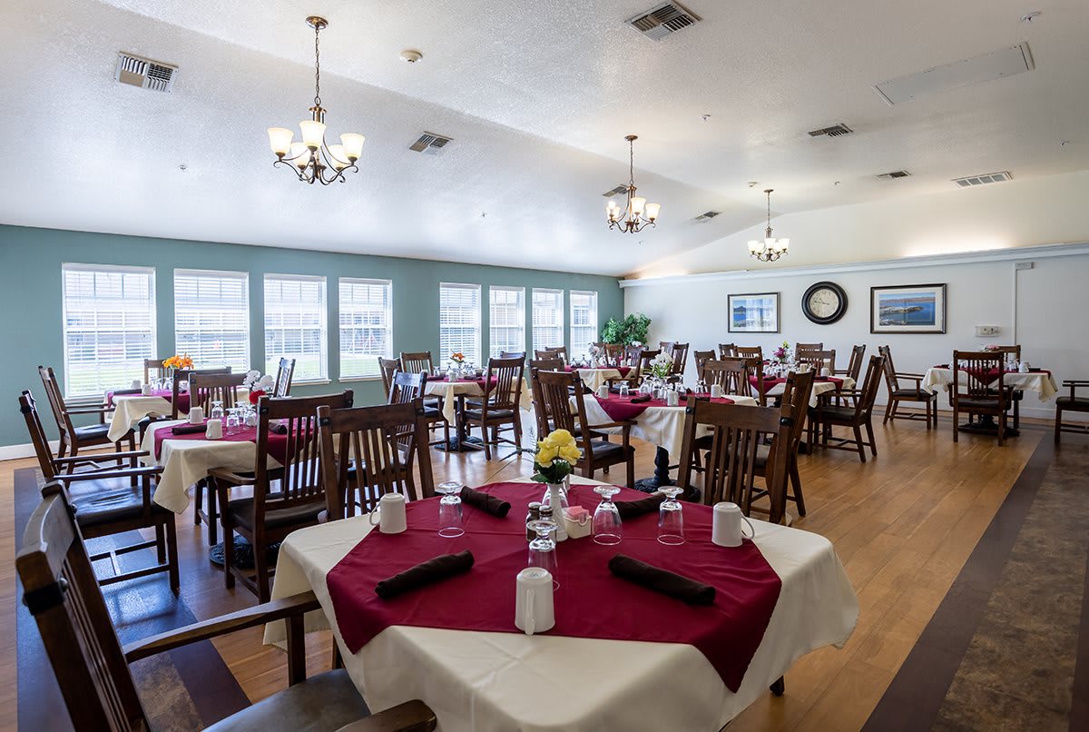A spacious dining room with neatly arranged tables and chairs, adorned with chandeliers and large windows.