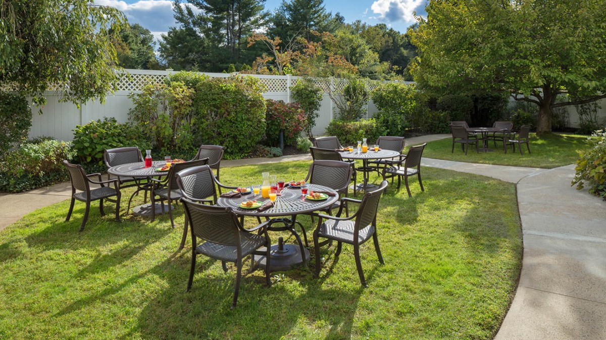 Outdoor dining area set in a garden with tables and chairs on a sunny day.