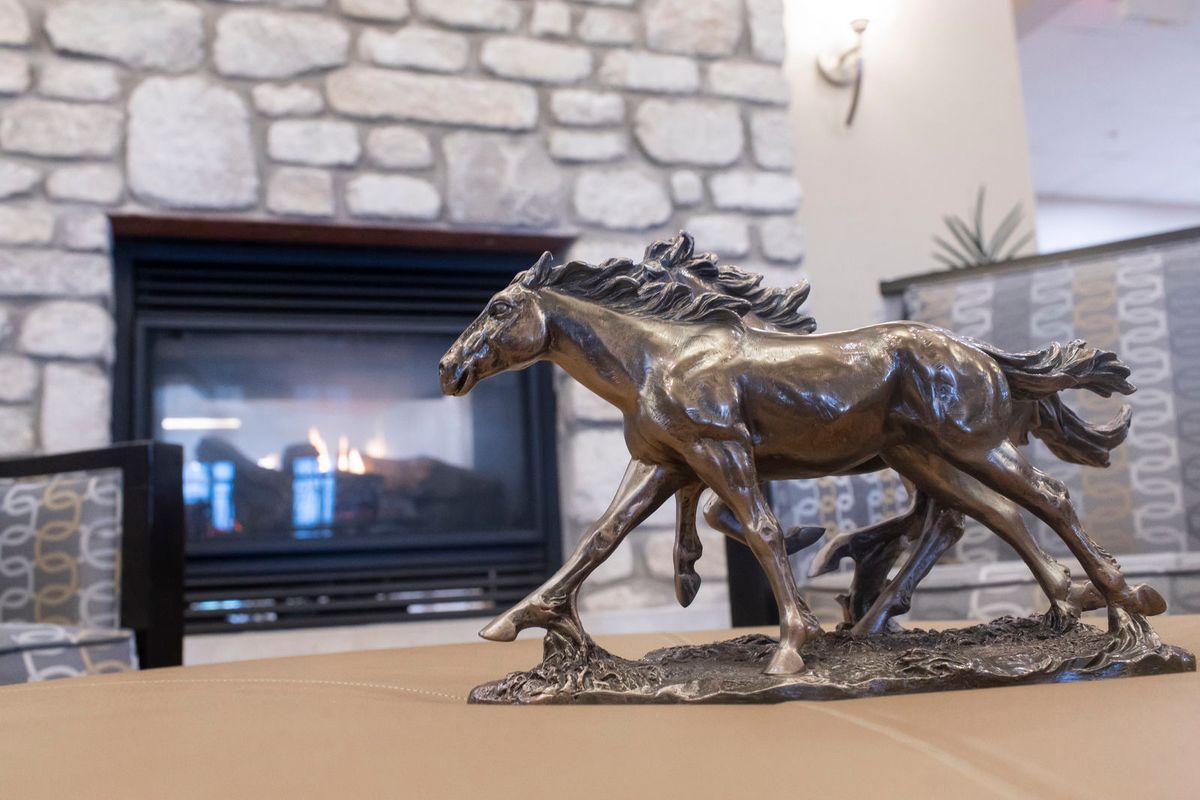 A bronze horse sculpture placed in front of a stone fireplace.