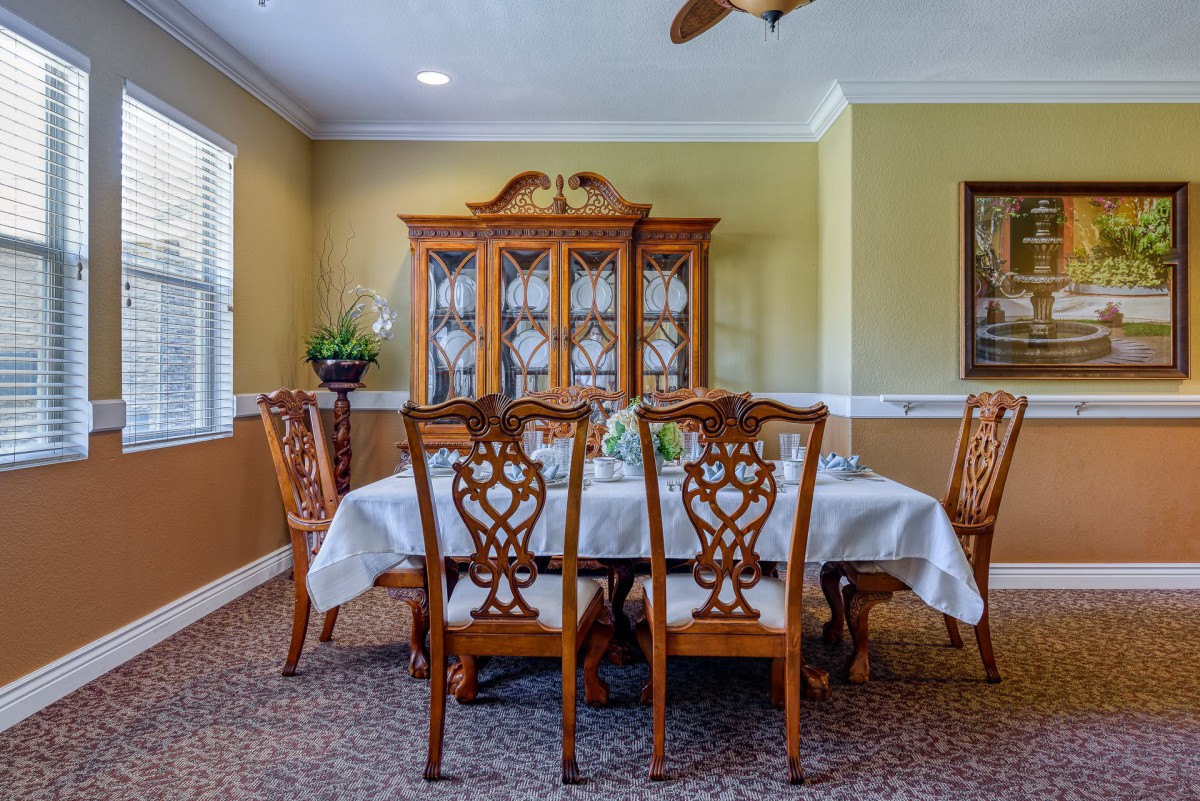 A classic dining room with a wooden table and intricately designed chairs, featuring a china cabinet in the background.