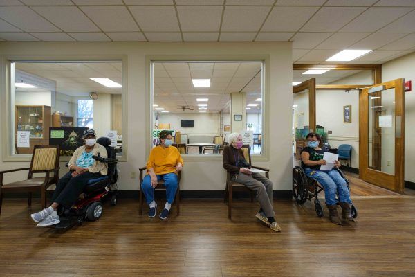 People seated in a medical facility waiting room, some in wheelchairs and wearing masks.