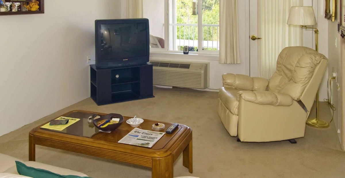 A cozy living room with a television, beige armchair, and a wooden coffee table.
