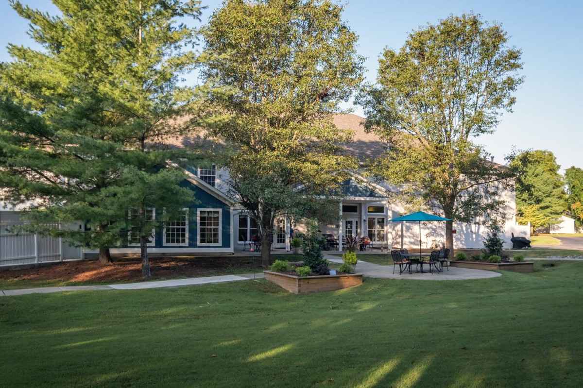 A beautiful house with a spacious lawn and patio surrounded by trees.