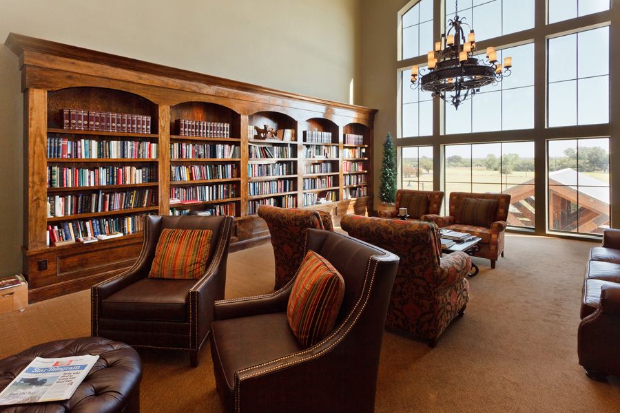 A cozy library space with armchairs and tall bookshelves, illuminated by natural light from a large window.
