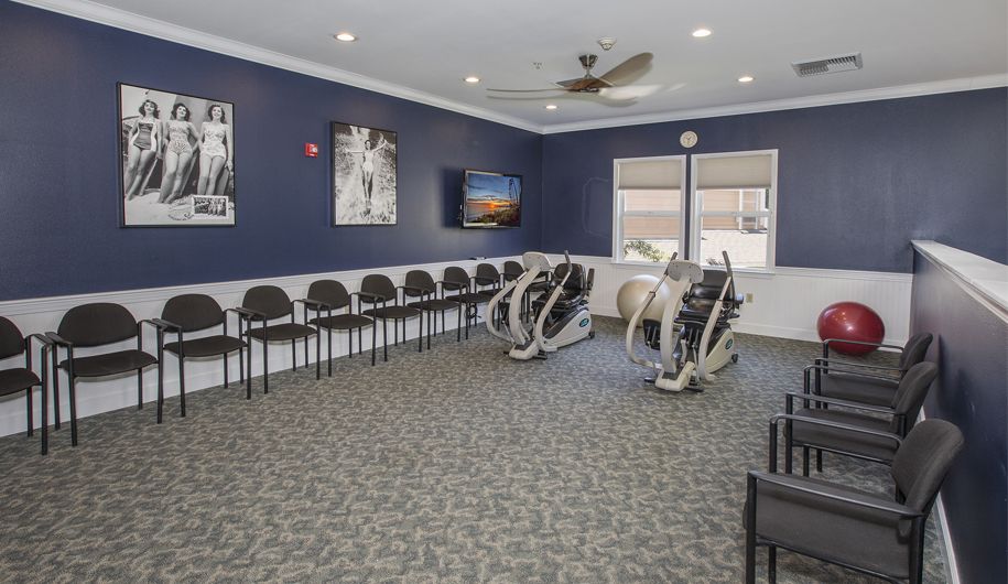 A fitness room with exercise machines, chairs lined up against the walls, and a television mounted on a navy blue wall.