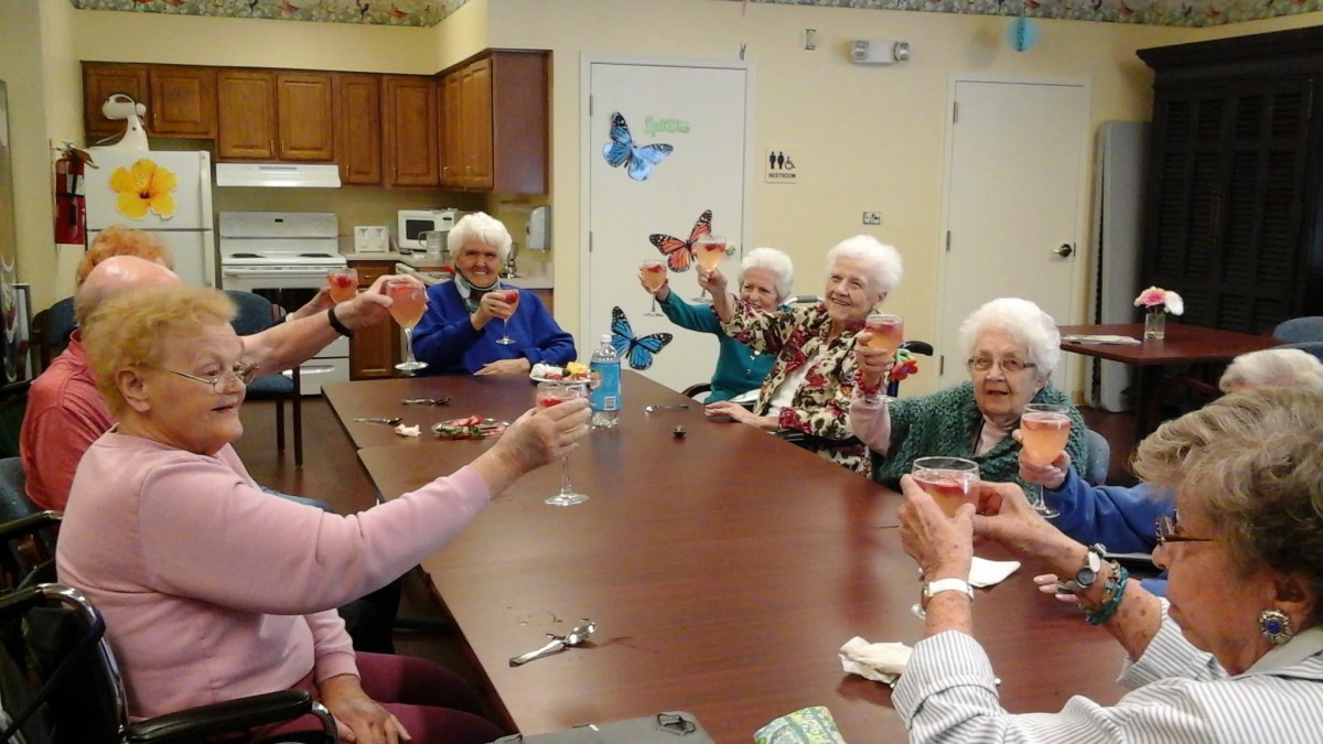 A group of elderly women enjoying a celebration, toasting at a table indoors.