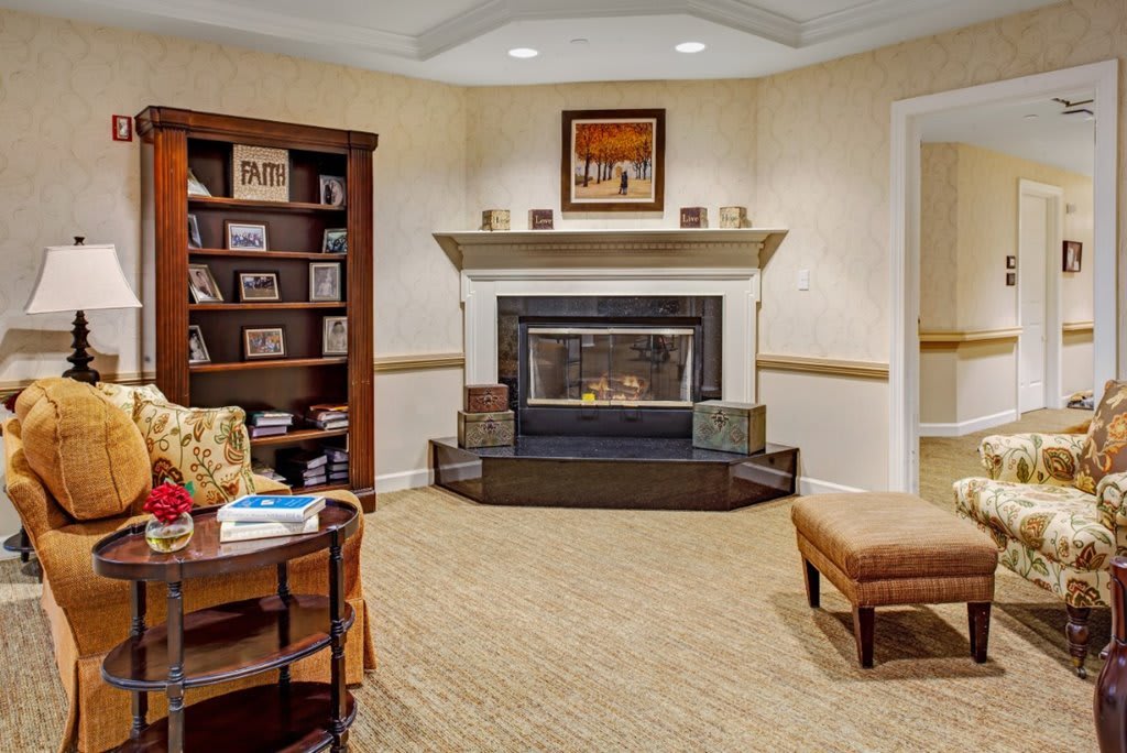 A cozy living room with a fireplace and bookshelf, featuring comfortable seating and warm interior design.