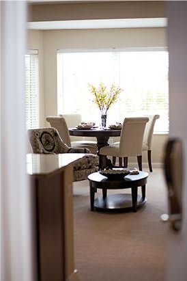 A cozy dining room with a round table, surrounded by chairs, and a vase with flowers as the centerpiece.