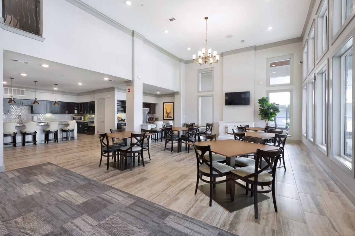 A modern, spacious dining area with multiple tables and chairs, featuring a high ceiling and a chandelier, bathed in natural light.