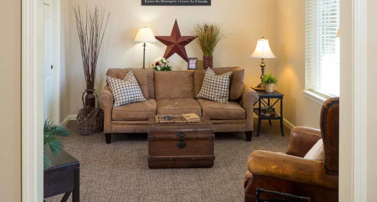A cozy living room with a brown sofa, decorative cushions, a wooden coffee table, and warm lighting from table lamps.