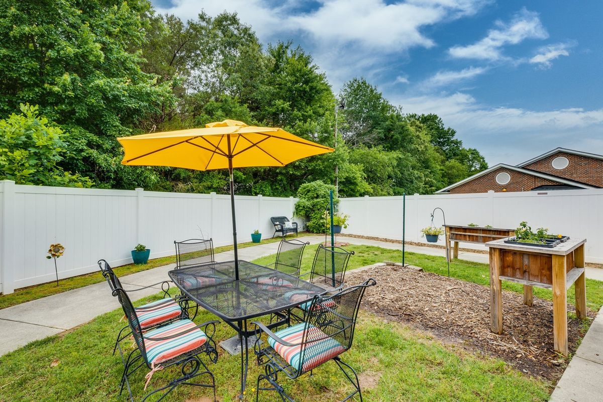 A sunny backyard patio with a table, chairs, and a yellow umbrella.