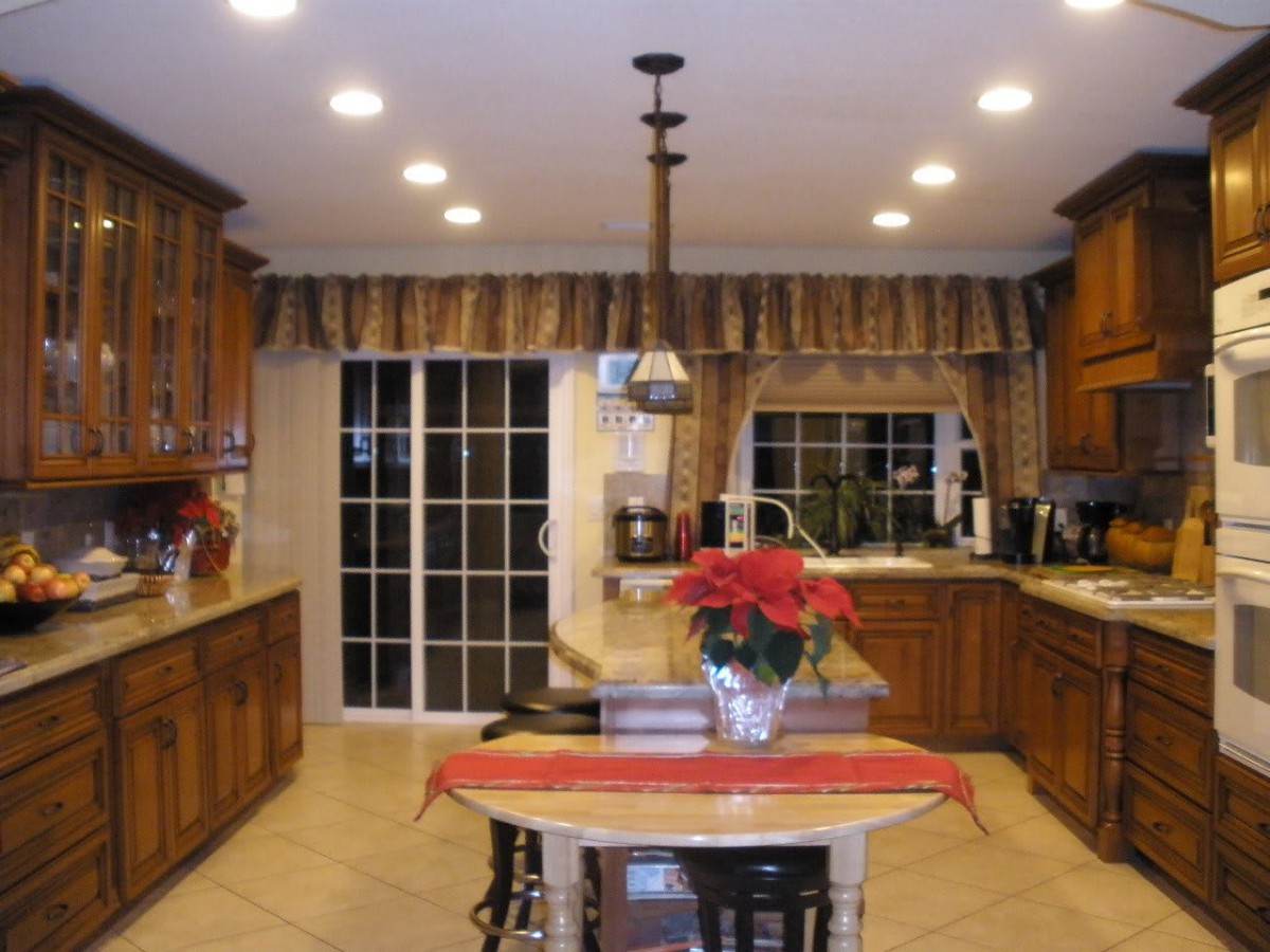 A modern kitchen interior featuring wooden cabinets, an island with a poinsettia centerpiece, and bright overhead lighting.