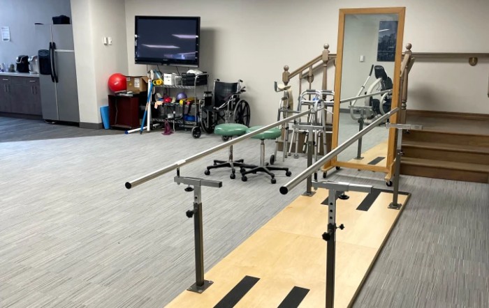 A physical therapy room equipped with parallel bars and various rehabilitation tools.