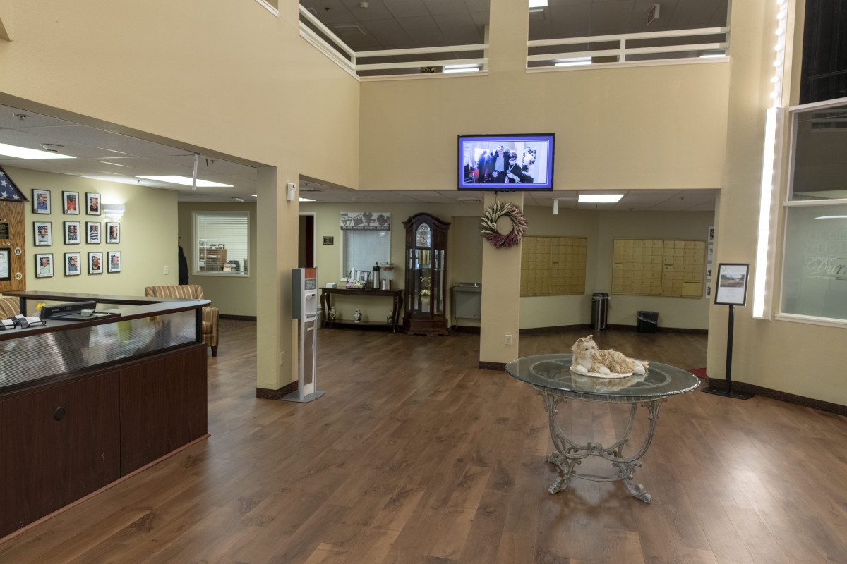 A modern lobby with a reception area, featuring a wooden floor, glass tables, and a wall-mounted television.