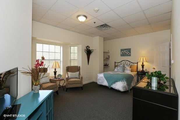 A cozy bedroom with stylish decor, featuring a bed, two chairs by the window, and ambient lighting.