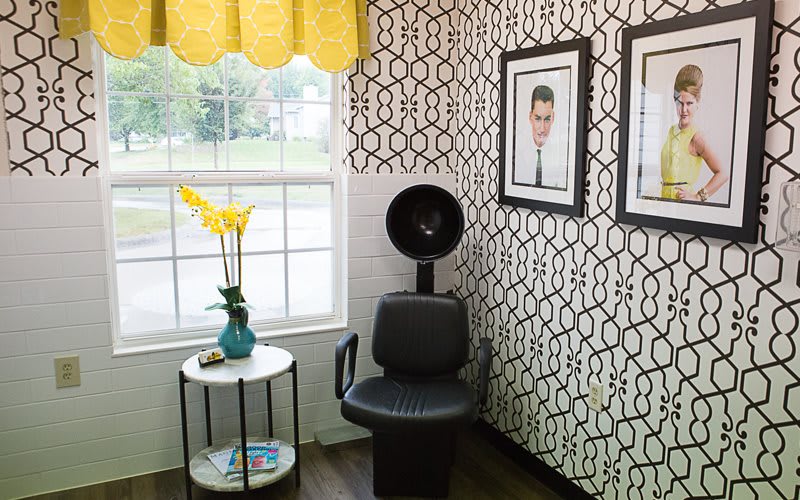 A stylish salon corner with a hair dryer chair, modern wallpaper, and decorative wall art.