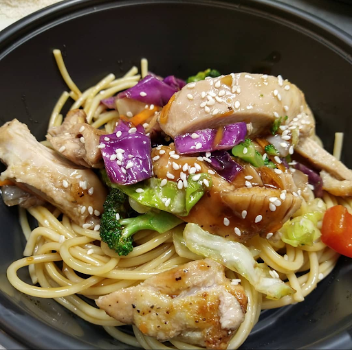 A delicious bowl of chicken stir-fried noodles with fresh vegetables and sesame seeds.