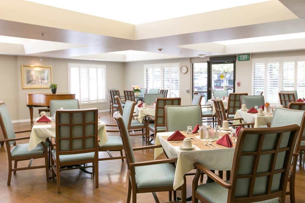A bright and neatly arranged dining room with multiple set tables and chairs.