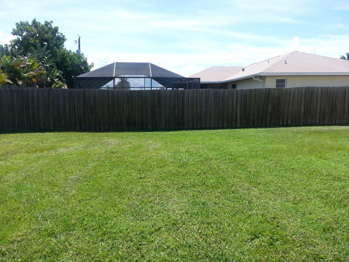 A neatly mowed backyard with a wooden fence and houses in the background.