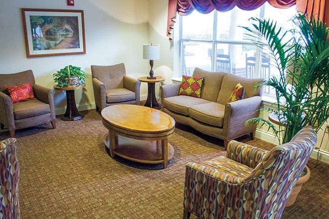 A cozy living room with a sofa, armchairs, a wooden coffee table, and a floor lamp, featuring an indoor plant by the window.