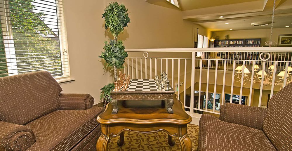 A cozy indoor setting featuring a chess board on a wooden table, complemented by comfortable seating and a decorative plant.
