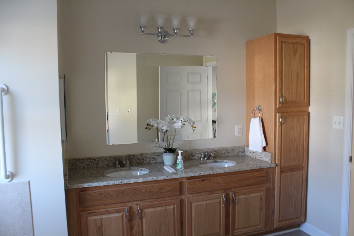 A bathroom featuring a double vanity with mirrors, wooden cabinets, and an orchid decoration.