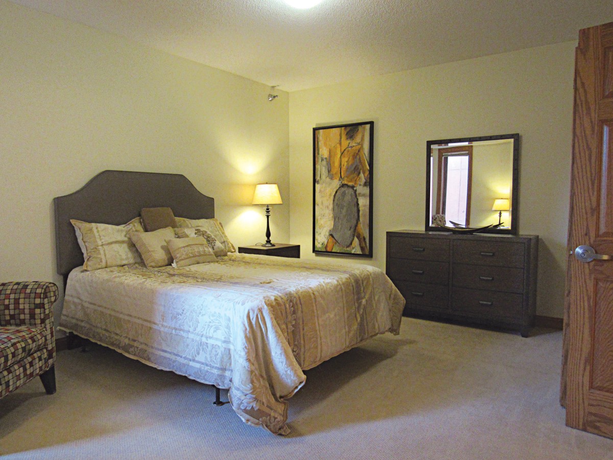 A cozy bedroom featuring a bed with decorative pillows, two bedside lamps, a dresser with a mirror, and artwork on the wall.