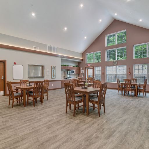 A spacious dining area with wooden tables and chairs, featuring high ceilings and large windows that let in ample natural light.