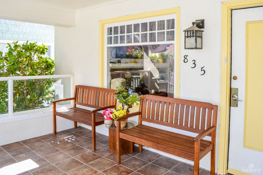 A cozy porch featuring wooden benches and decorative flower pots next to a large window.